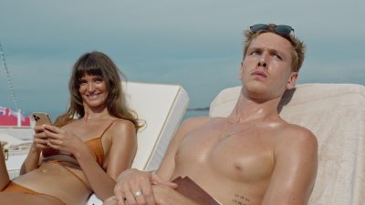 En bild ur en filmscen där två personer solar.